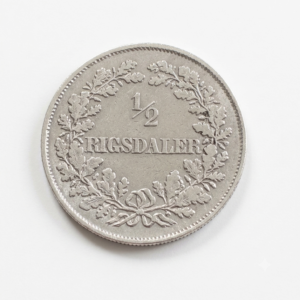 Close-up of a silver half‑rigsdaler coin surrounded by a laurel wreath with '1/2 RIGSDALER' inscribed.